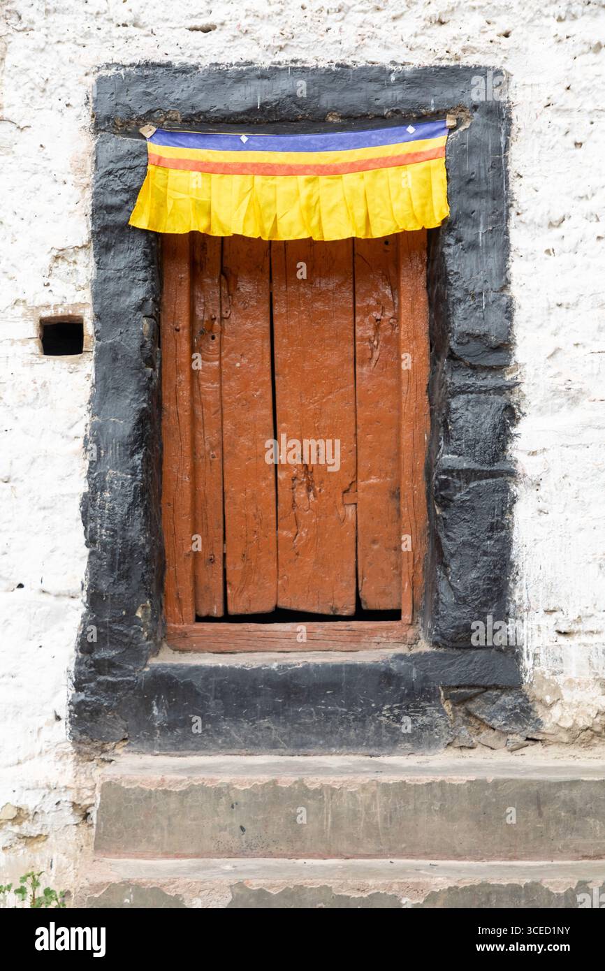 Una porta in legno rustica adornata con un vivace tessuto giallo, rosso e blu nella valle di Zanskar, Ladakh, India, che mostra il tradizionale arco himalayano Foto Stock