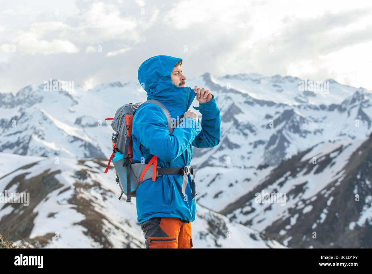Un uomo con una giacca blu sta facendo trekking attraverso le cime innevate dei Pirenei. Con uno zaino e l'equipaggiamento protettivo, esplora la splendida rete di montagna Foto Stock