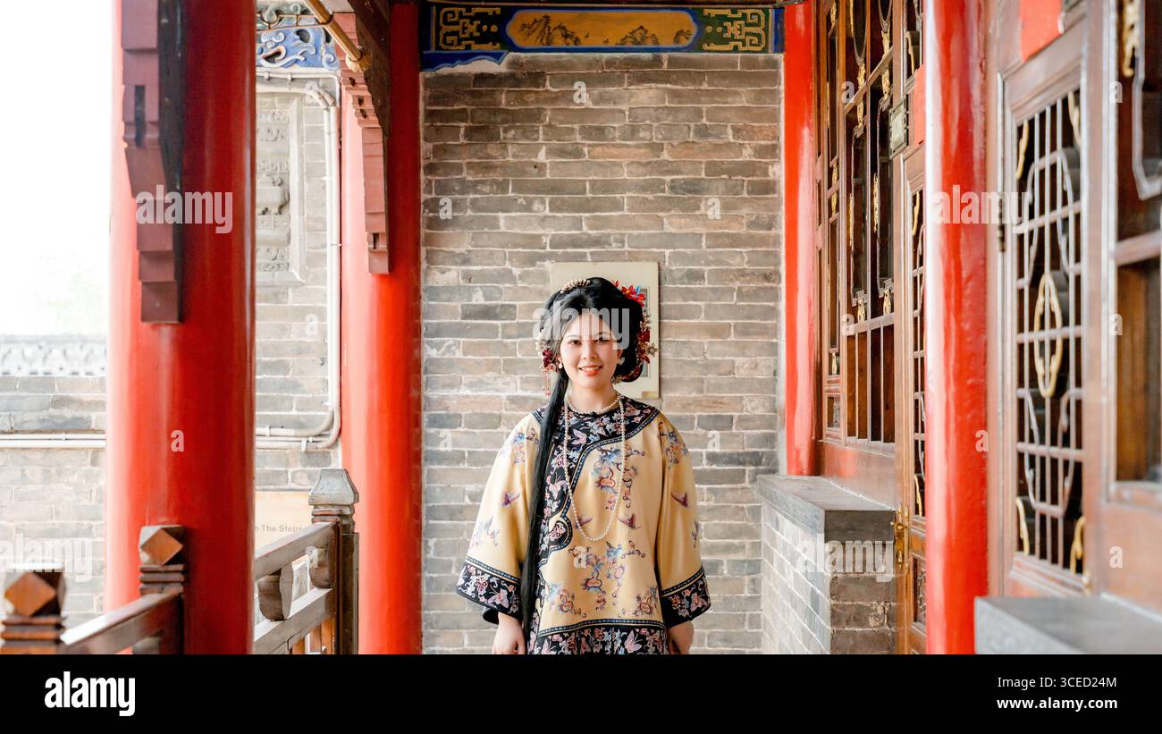Una donna vestita con abiti tradizionali della dinastia Qing si trova a Pingyao, in Cina, guardando la macchina fotografica. L'ambientazione storica mette in risalto la ricca storia della Cina Foto Stock