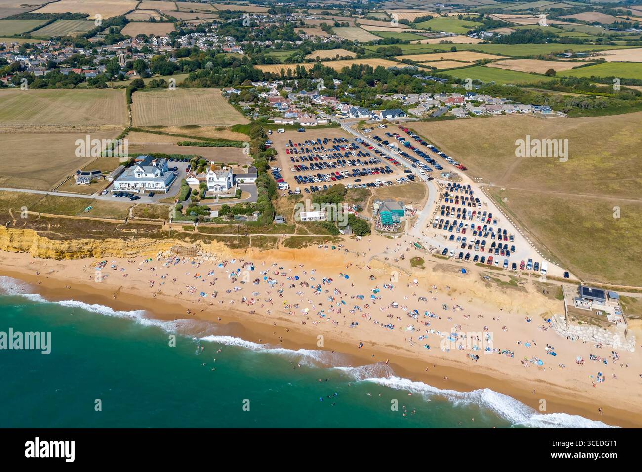 Burton Bradstock, Dorset, Regno Unito. 17 agosto 2025. Meteo nel Regno Unito. La spiaggia e il parcheggio sono pieni di turisti che si godono il caldo sole e il cielo azzurro dell'Hive Beach a Burton Bradstock, sulla Dorset Jurassic Coast, circondata da campi tormentati dalla siccità, mentre l'ondata di caldo continua durante le vacanze estive. Crediti fotografici: Graham Hunt/Alamy Live News Foto Stock