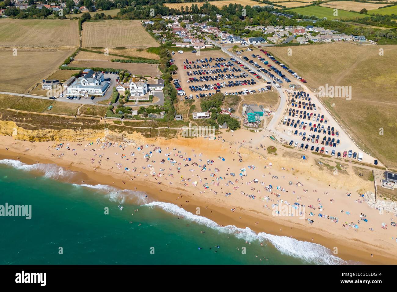 Burton Bradstock, Dorset, Regno Unito. 17 agosto 2025. Meteo nel Regno Unito. La spiaggia e il parcheggio sono pieni di turisti che si godono il caldo sole e il cielo azzurro dell'Hive Beach a Burton Bradstock, sulla Dorset Jurassic Coast, circondata da campi tormentati dalla siccità, mentre l'ondata di caldo continua durante le vacanze estive. Crediti fotografici: Graham Hunt/Alamy Live News Foto Stock