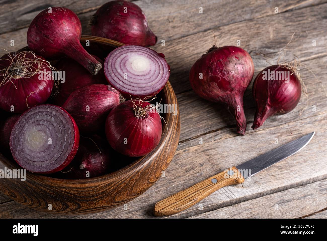 Cipolla rossa in una ciotola di legno su fondo di legno con coltello Foto Stock