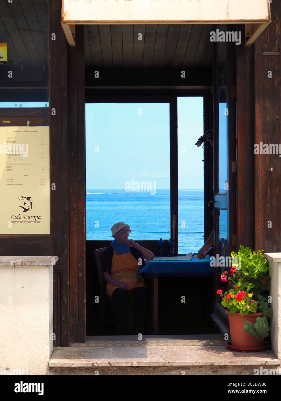 Anziana donna seduta all'interno del ristorante sul mare Lido Europa con vista mare a Taormina, Sicilia Foto Stock