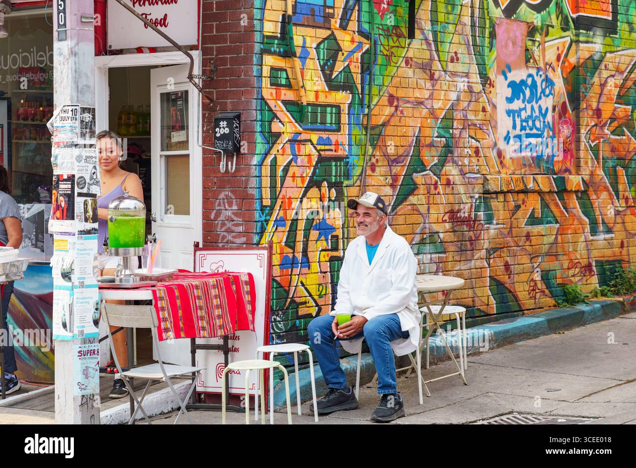 Un uomo siede con un drink fuori da un punto di ristoro peruviano, con colorati graffiti sul muro nel mercato di Kensington. Foto Stock