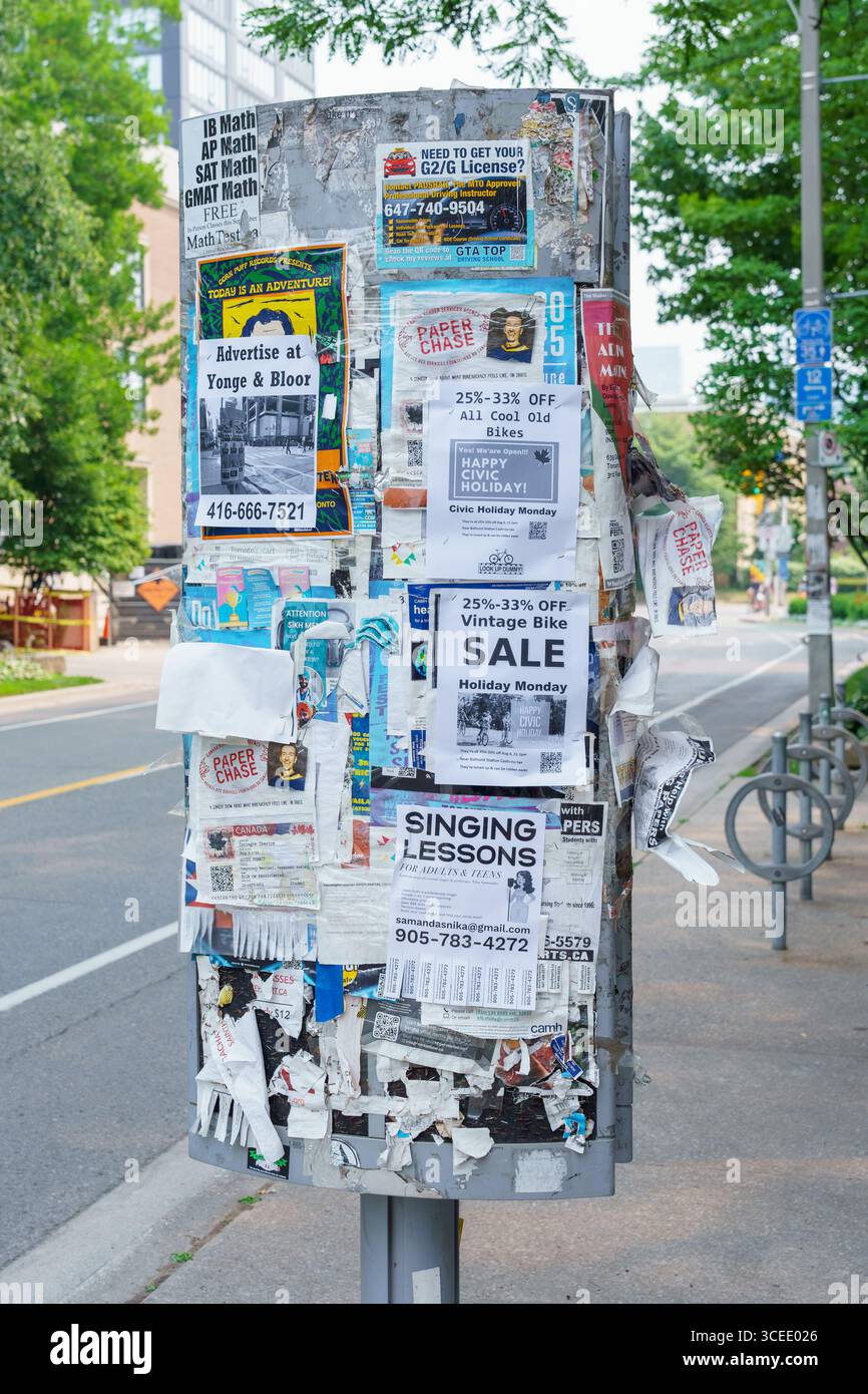 Un palo ricoperto da poster a strati e annunci si trova su un marciapiede Foto Stock
