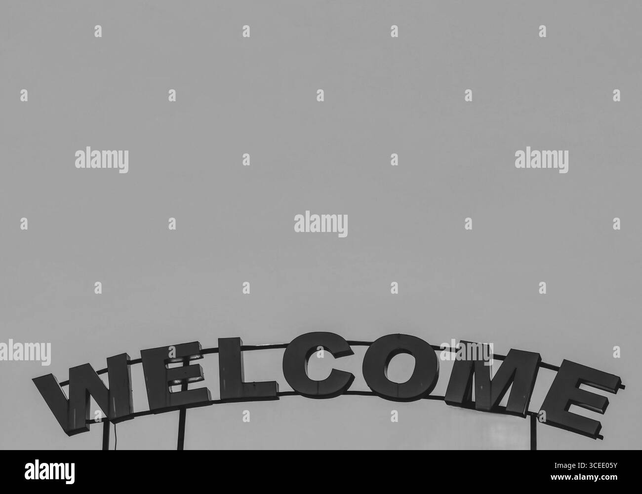 Benvenuto qui sopra. Segno metallico e cielo come spazio negativo. Tonalità monocromatiche. Foto Stock