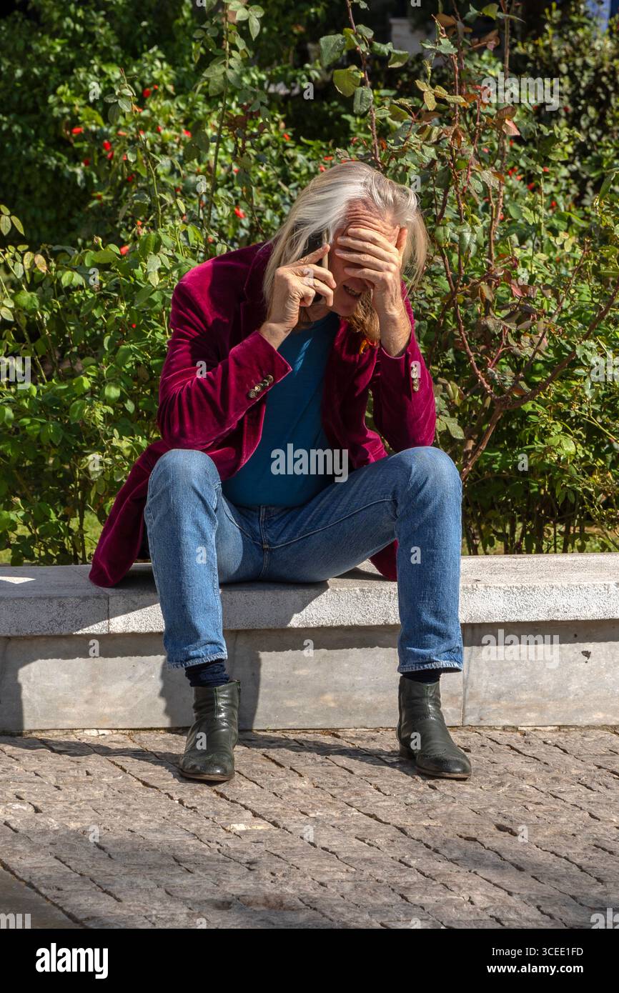 Uomo che sembra in disordine mentre usa il telefono per strada, Atene, Grecia Foto Stock