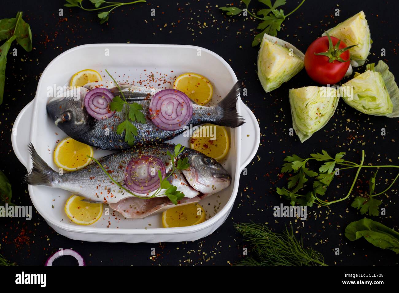 Pronti per cucinare due orate marinate intere su una superficie nera con ingredienti. Vista dall'alto Foto Stock