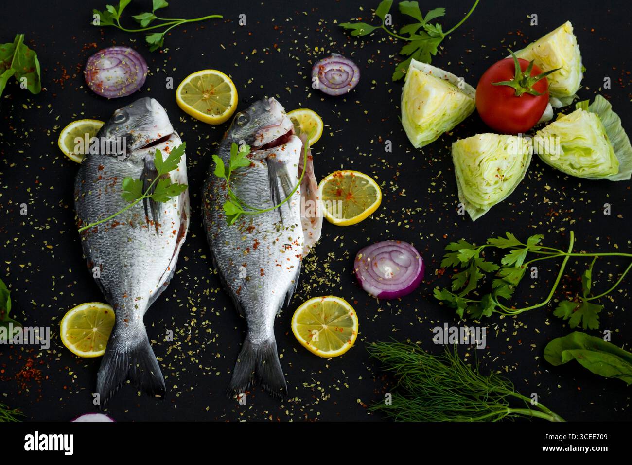 Pronti per cucinare due orate marinate intere su una superficie nera con ingredienti. Vista dall'alto Foto Stock