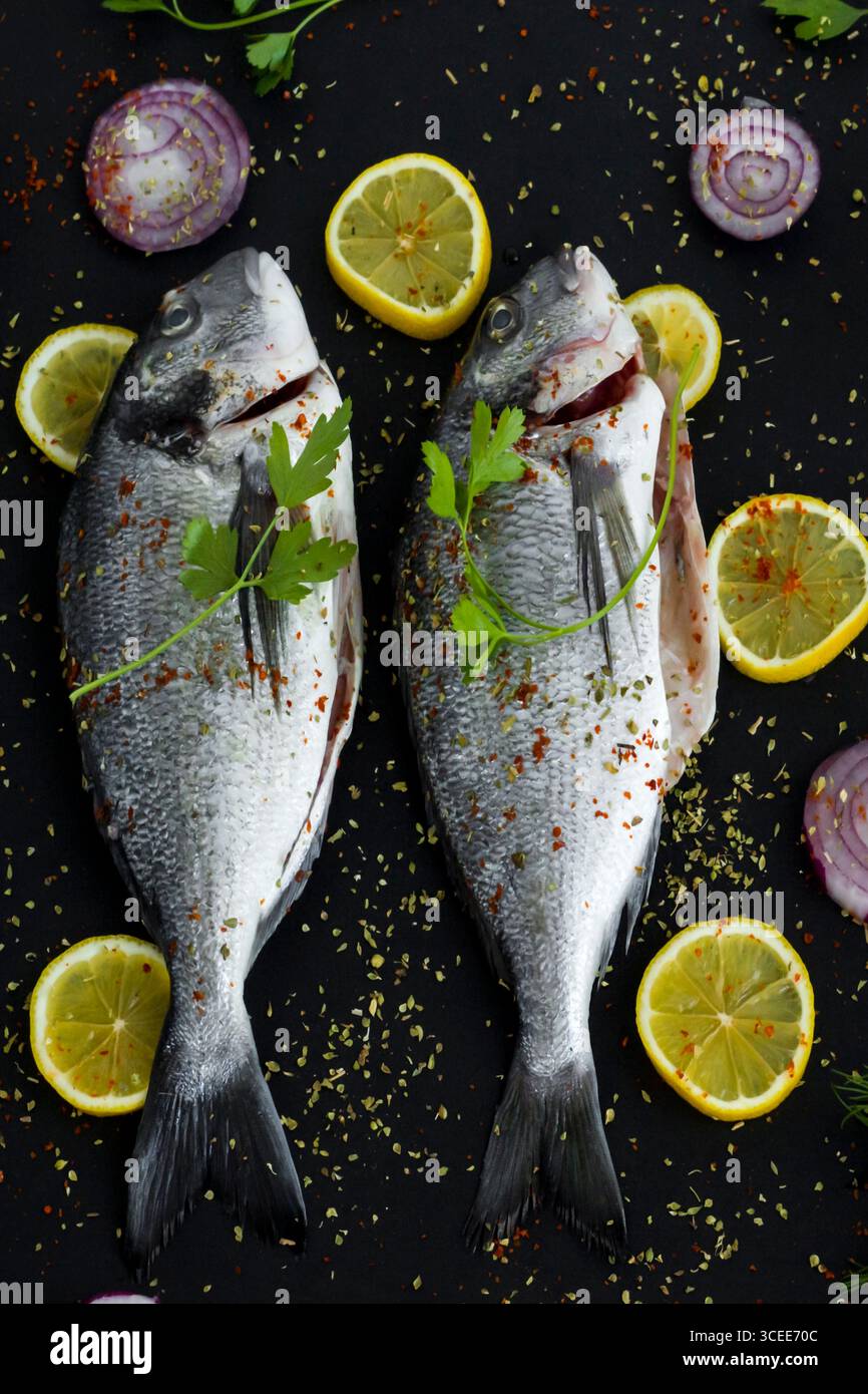 Pronti per cucinare due orate marinate intere su una superficie nera con ingredienti. Vista dall'alto Foto Stock