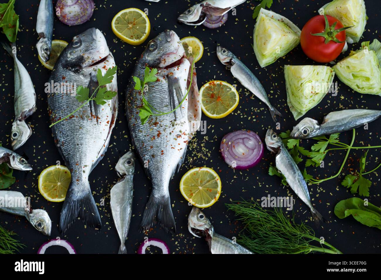 Pronti per cucinare due orate marinate intere su una superficie nera con ingredienti. Vista dall'alto Foto Stock
