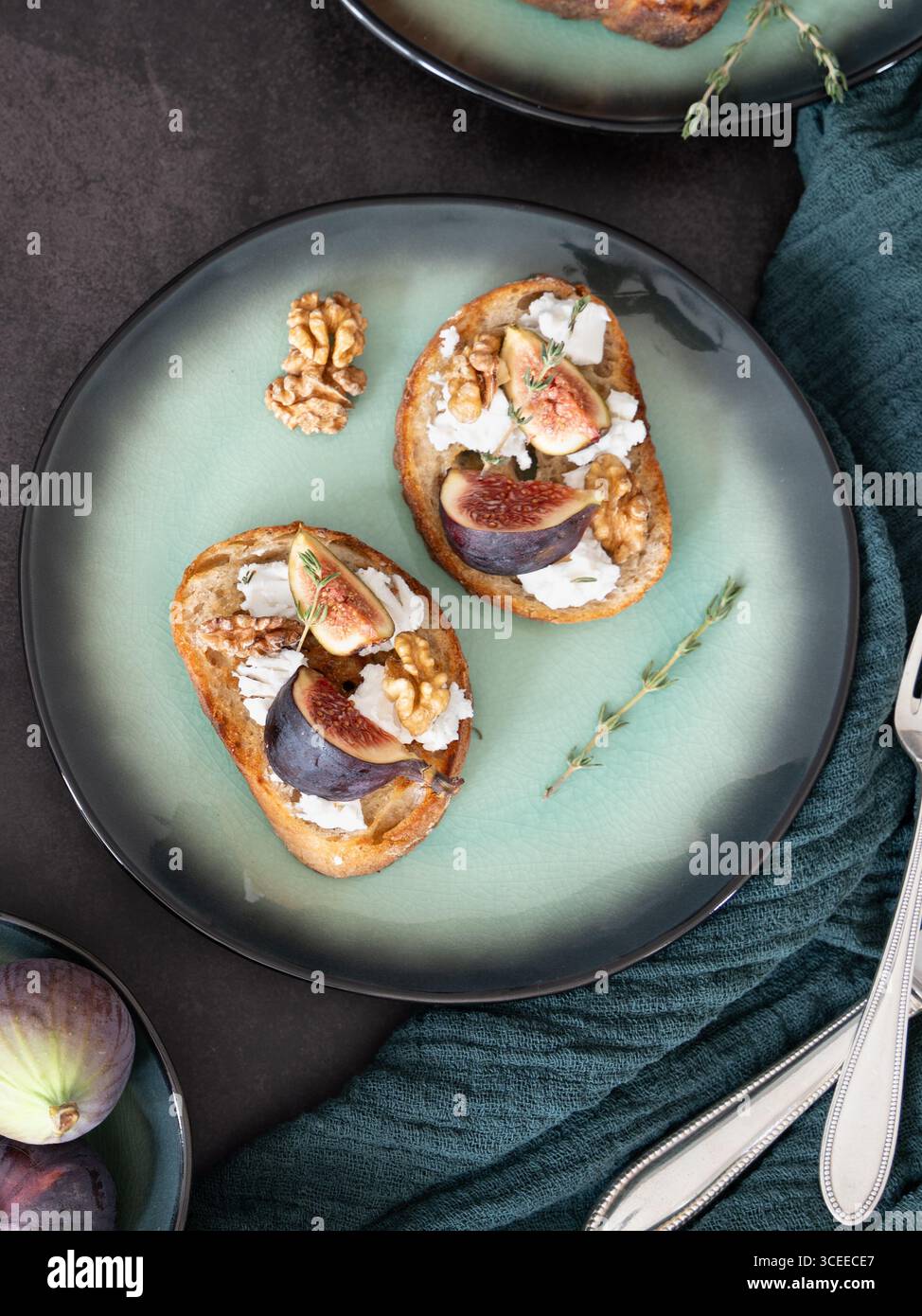 Vista dall'alto verticale ravvicinata di toast rustici di fico di capra con timo e noci su piatto verde e asciugamano Foto Stock