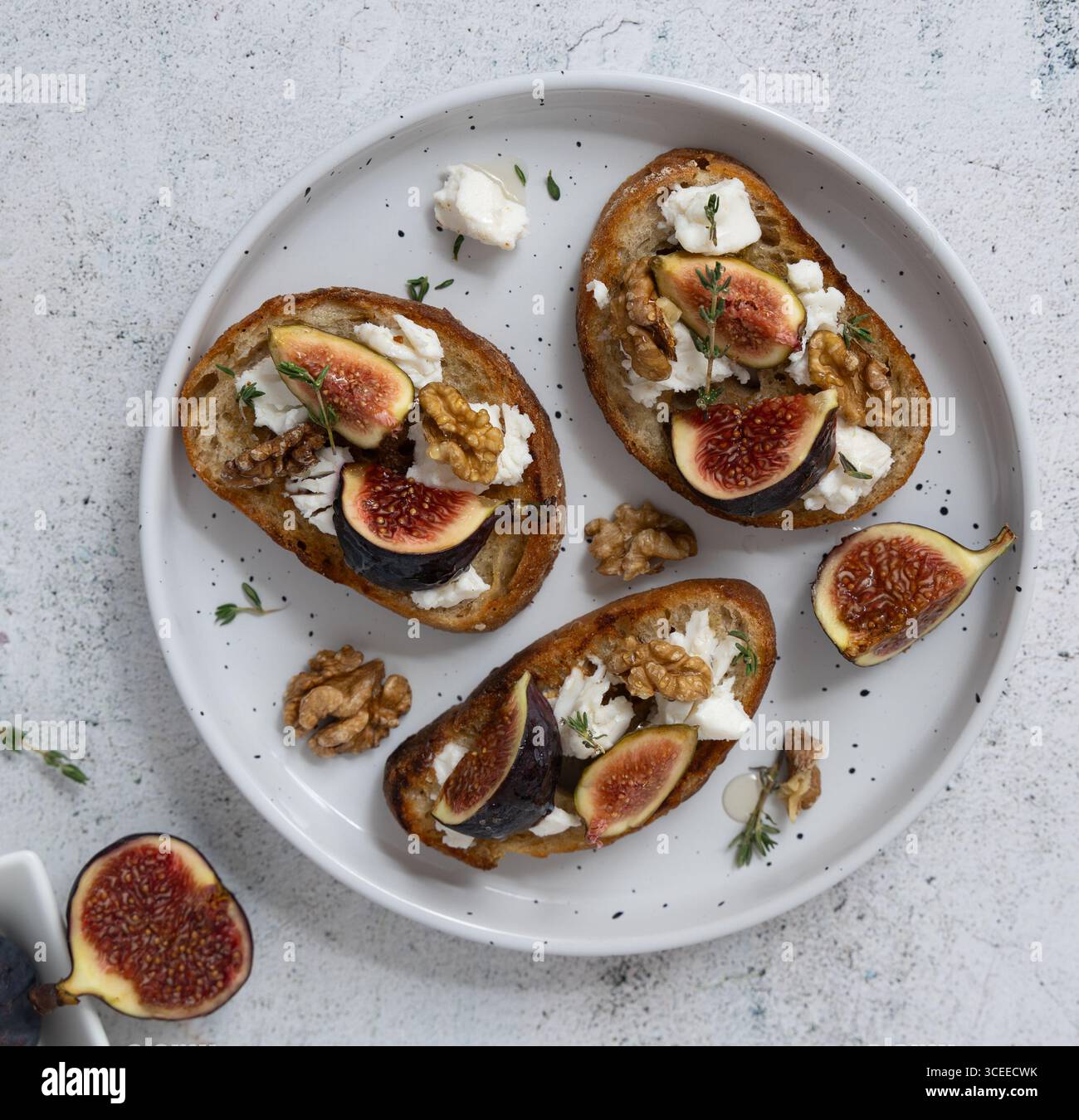Vista dall'alto orizzontale primo piano di tre toast di fichi e capra su un piatto bianco con timo, fichi su un piatto separato, mix salato e dolce Foto Stock