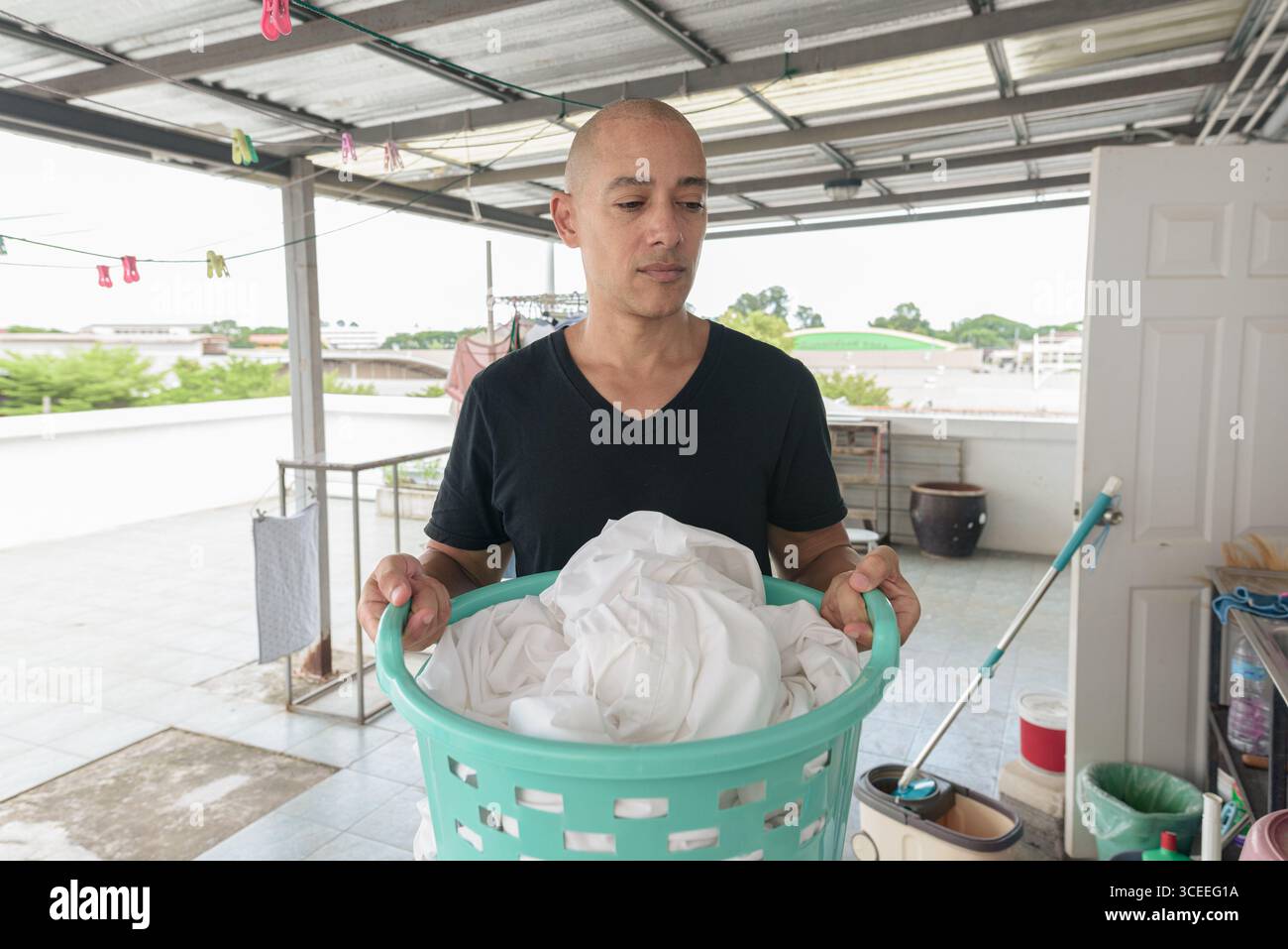 Uomo multietnico di mezza età con t-shirt nera, in piedi all'aperto con cesto per bucato in mano, che si prepara a caricare i vestiti nel lavacristallo mac Foto Stock