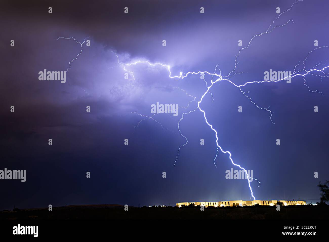Un enorme fulmine divide il cielo notturno sopra un complesso di appartamenti a Tucson, Arizona, catturando il potere grezzo delle tempeste monsoniche del deserto. Foto Stock