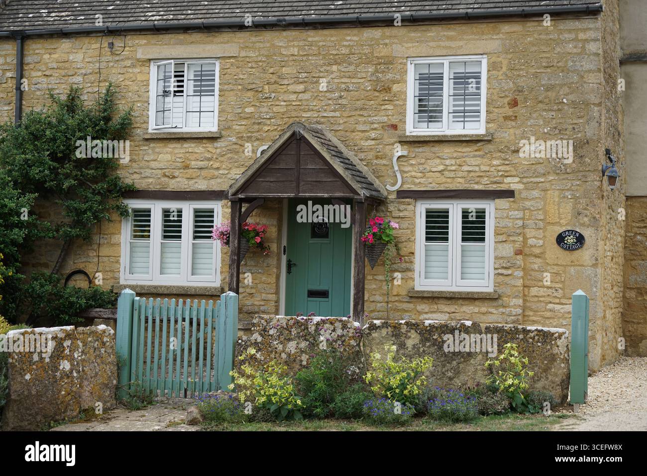 Incantevole cottage in pietra con cancello verde e decorazioni floreali. Piccola Rissington, Inghilterra Foto Stock