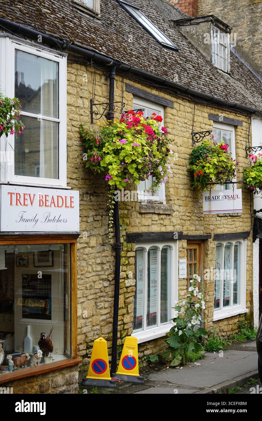 Affascinanti negozi in pietra del villaggio con colorati cesti di fiori appesi. Chipping Norton, Inghilterra Foto Stock