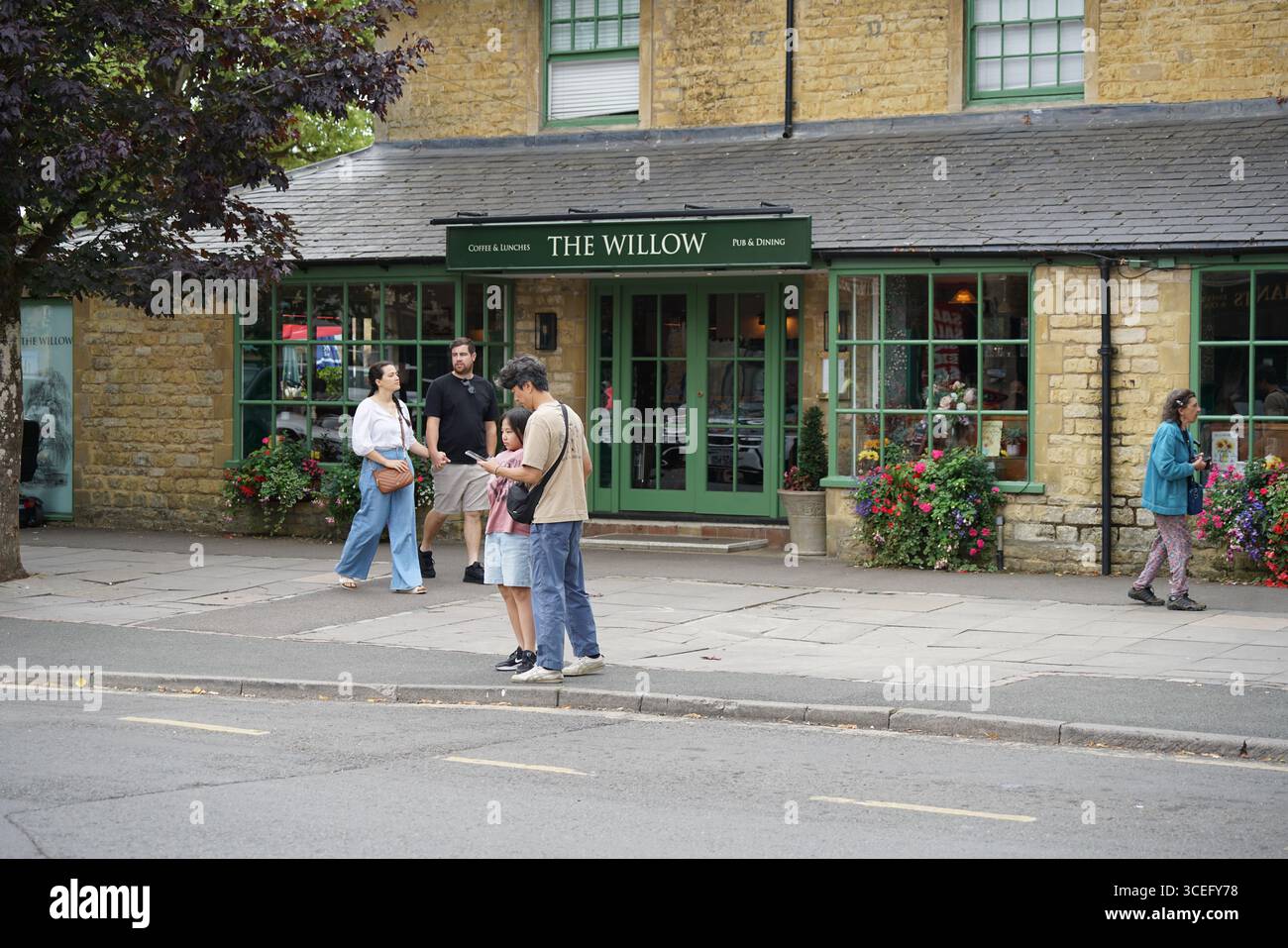 Vista sulla strada dell'esterno del pub Stone con persone in un abbigliamento informale. Bourton-on-the-Water, Inghilterra Foto Stock