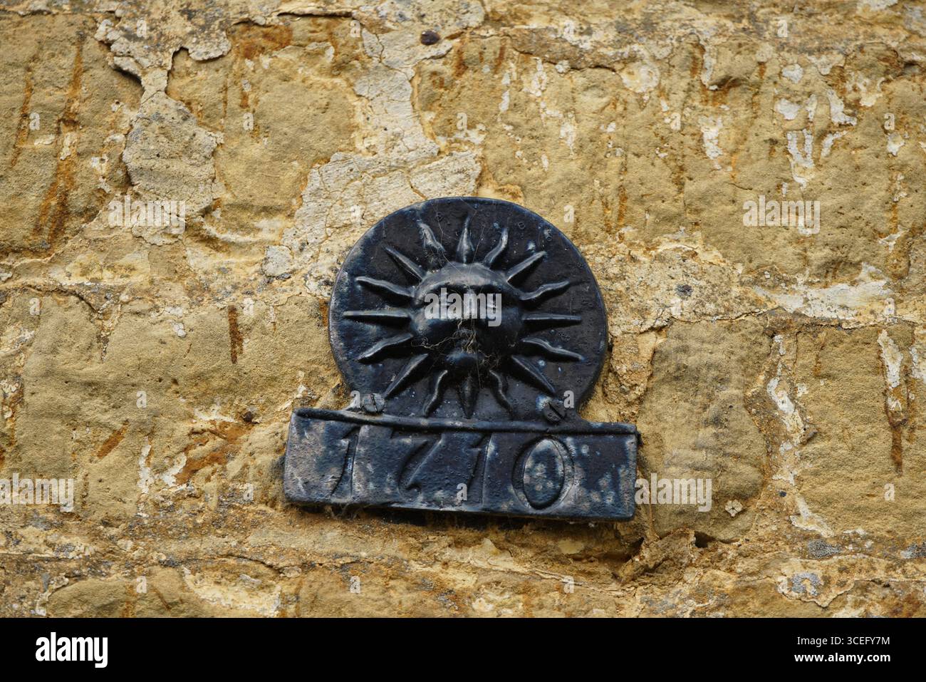 Placca in metallo antico con emblema solare su superficie a parete stucco invecchiata. Bourton-on-the-Water, Inghilterra Foto Stock