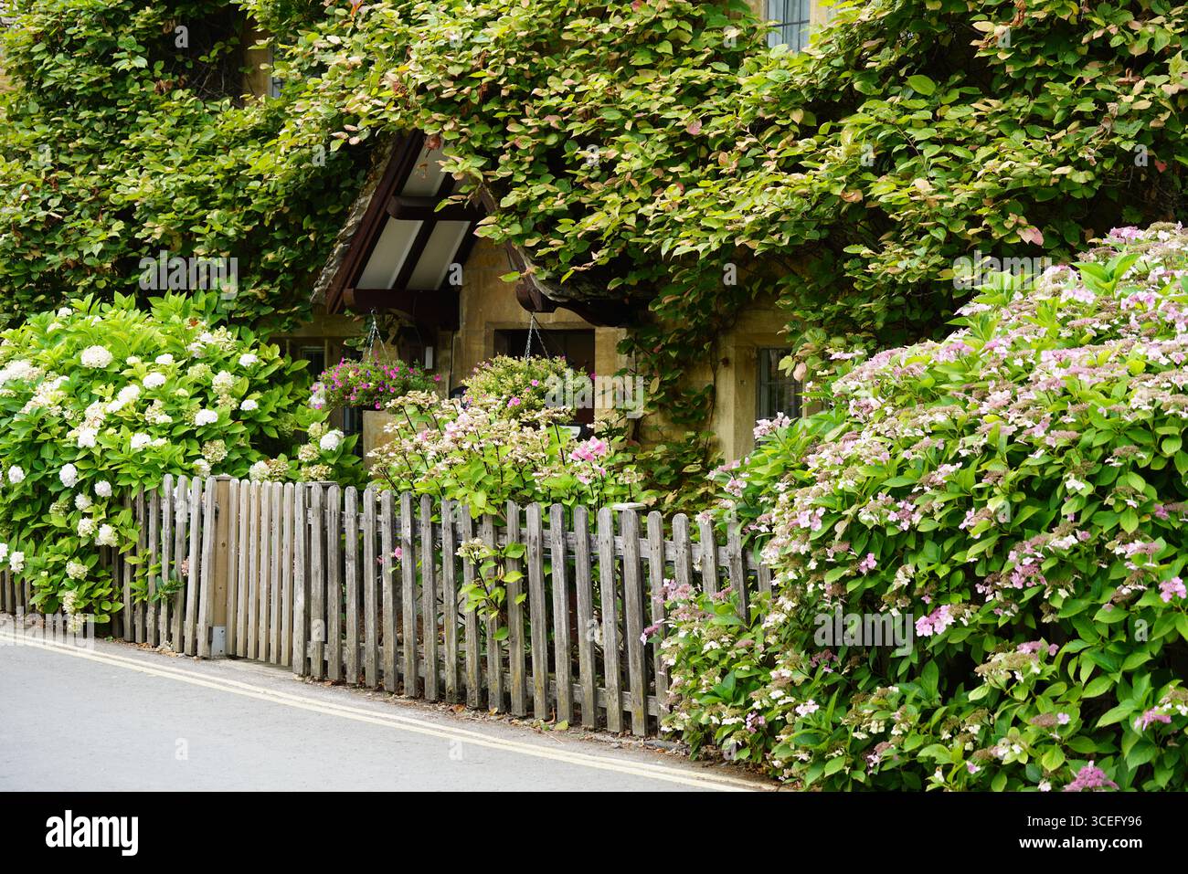 Affascinante Casa Rustica circondata da Giardino in fiore e recinzione in legno. Bourton-on-the-Water, Inghilterra Foto Stock