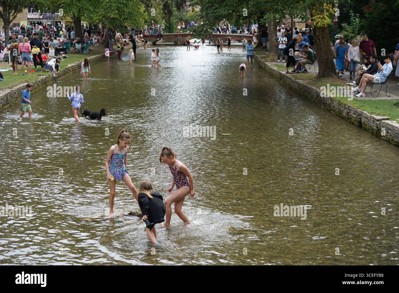 Le famiglie trascorrono una giornata divertente lungo un ruscello calmo in estate. Bourton-on-the-Water, Inghilterra Foto Stock