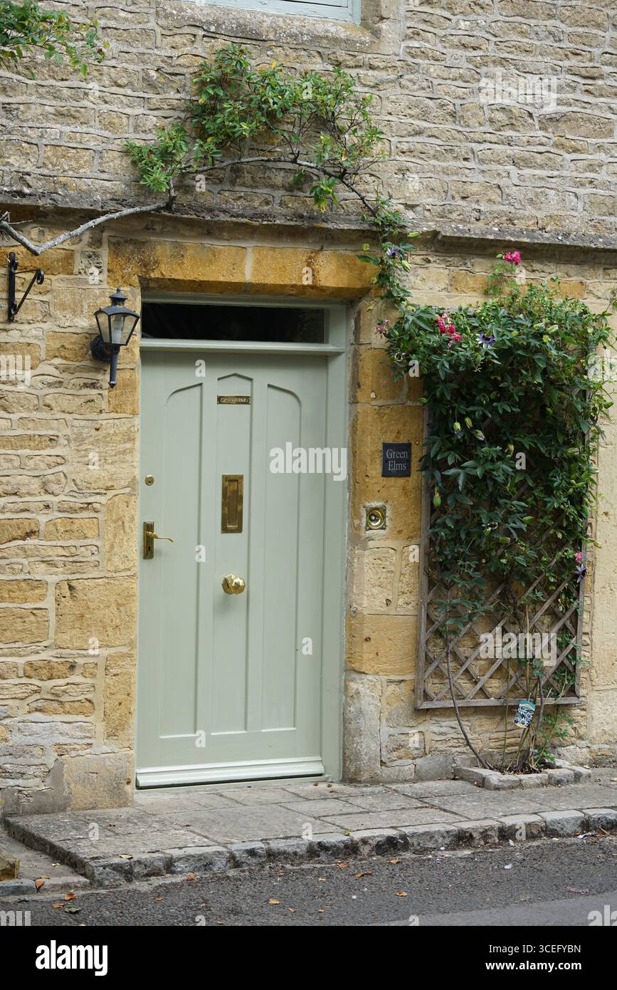 Affascinante casa in pietra con porta verde e ingresso incorniciato da edera in un ambiente pittoresco. Bourton-on-the-Water, Inghilterra Foto Stock