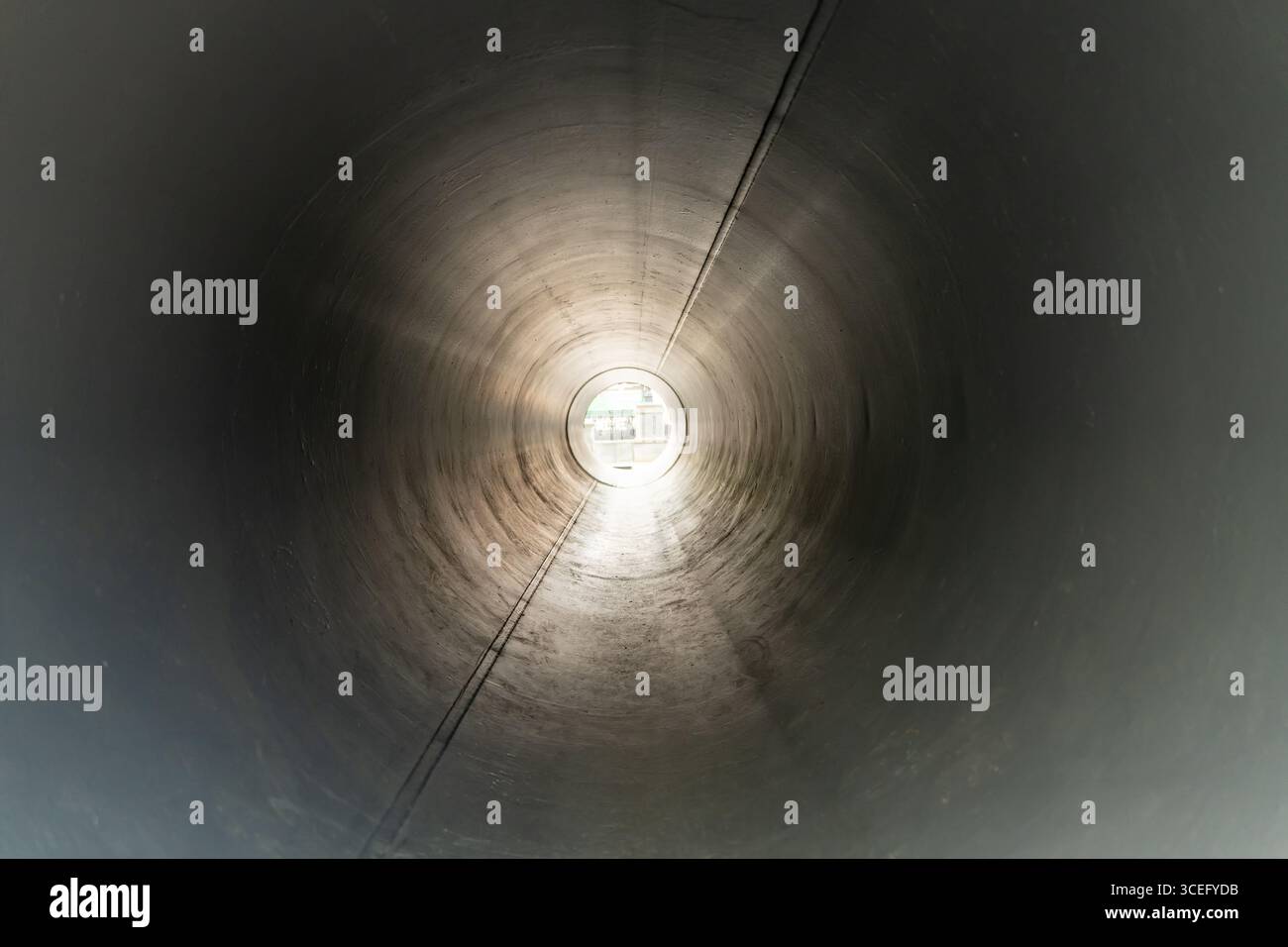 Vista interna di un grande tubo metallico o tunnel con luce solare che splende attraverso l'apertura distante. Prospettiva industriale che mostra struttura, simmetria e. Foto Stock