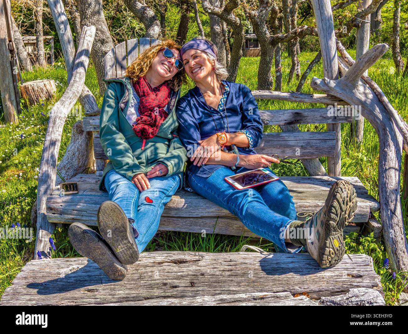 Due amiche donne sedute e sorridenti su un sedile costruito a mano a Hornby Island, British Columbia, Canada. Foto Stock