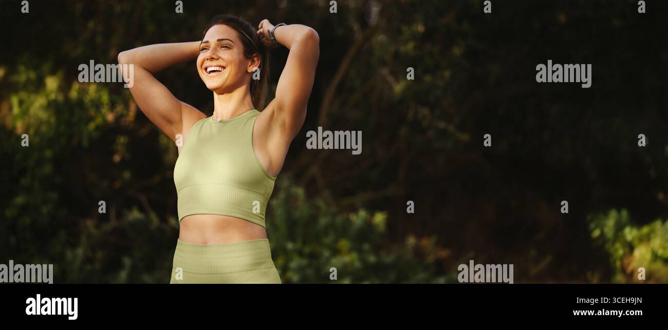 Mettete in forma la giovane donna in un abbigliamento sportivo sorridente e rilassante dopo l'esercizio fisico in un ambiente naturale all'aperto. Concetto di fitness, benessere, consapevolezza e un AC Foto Stock