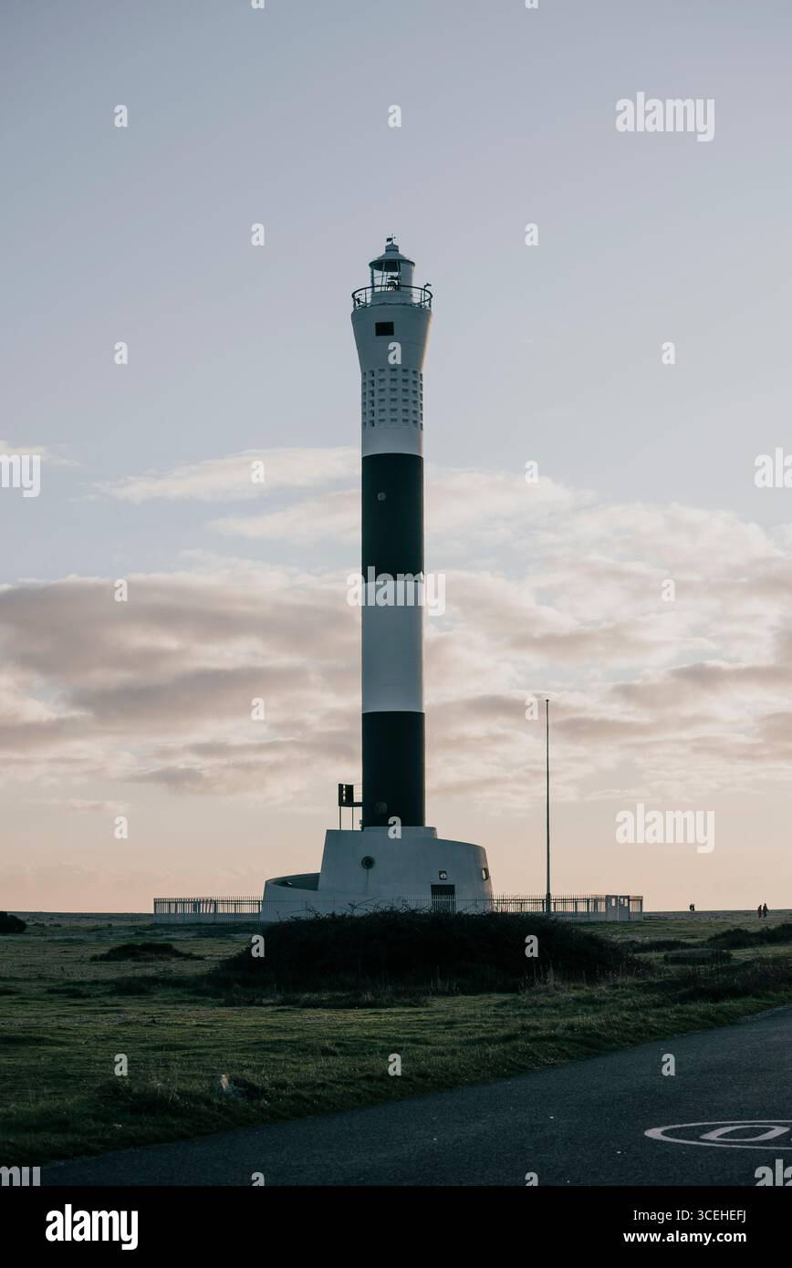 Un alto faro si erge da solo su una collina erbosa. Il cielo è limpido e il sole tramonta, proiettando un caldo bagliore sulla scena. Il faro è un simbolo Foto Stock