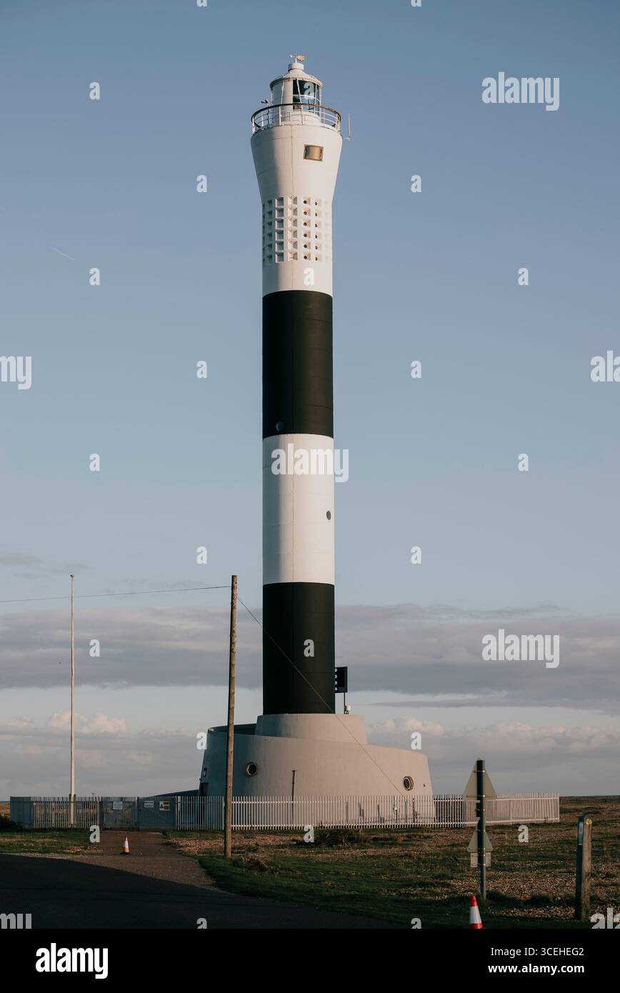 Un faro alto con una striscia bianca e nera. Il cielo è limpido e il sole splende Foto Stock
