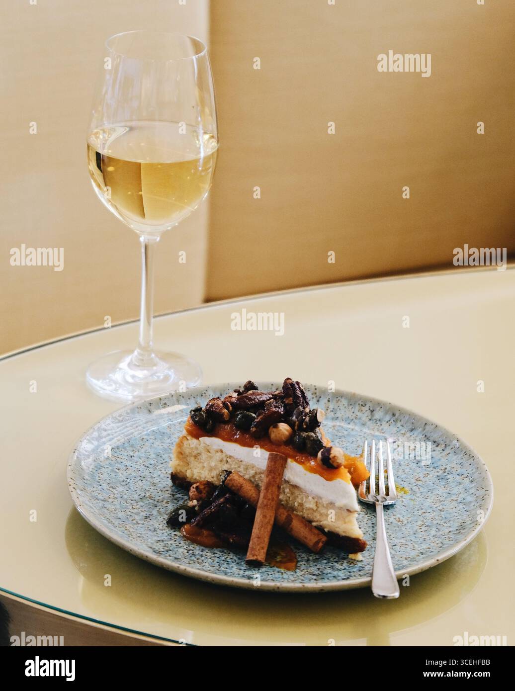 Dessert e bevande combinati, una fetta di cheesecake al caramello salato con noci caramellate su un piatto di ceramica blu e vino bianco. Elegante Foto Stock