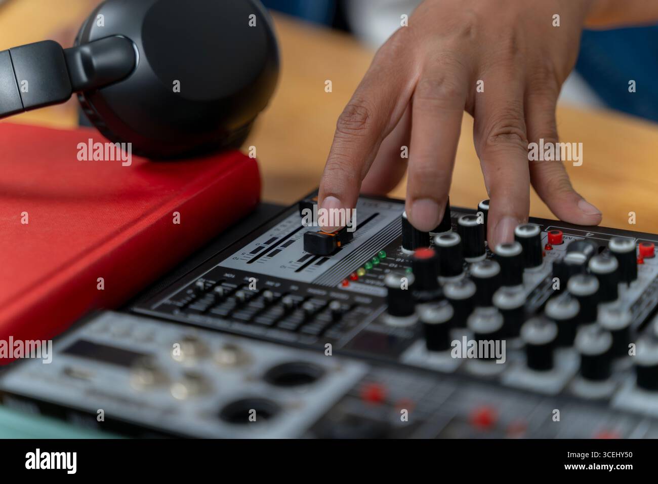 Vista ravvicinata di una mano che regola i livelli audio su un mixer audio, simboleggiando la registrazione di podcast, la trasmissione e la produzione audio moderna. Foto Stock