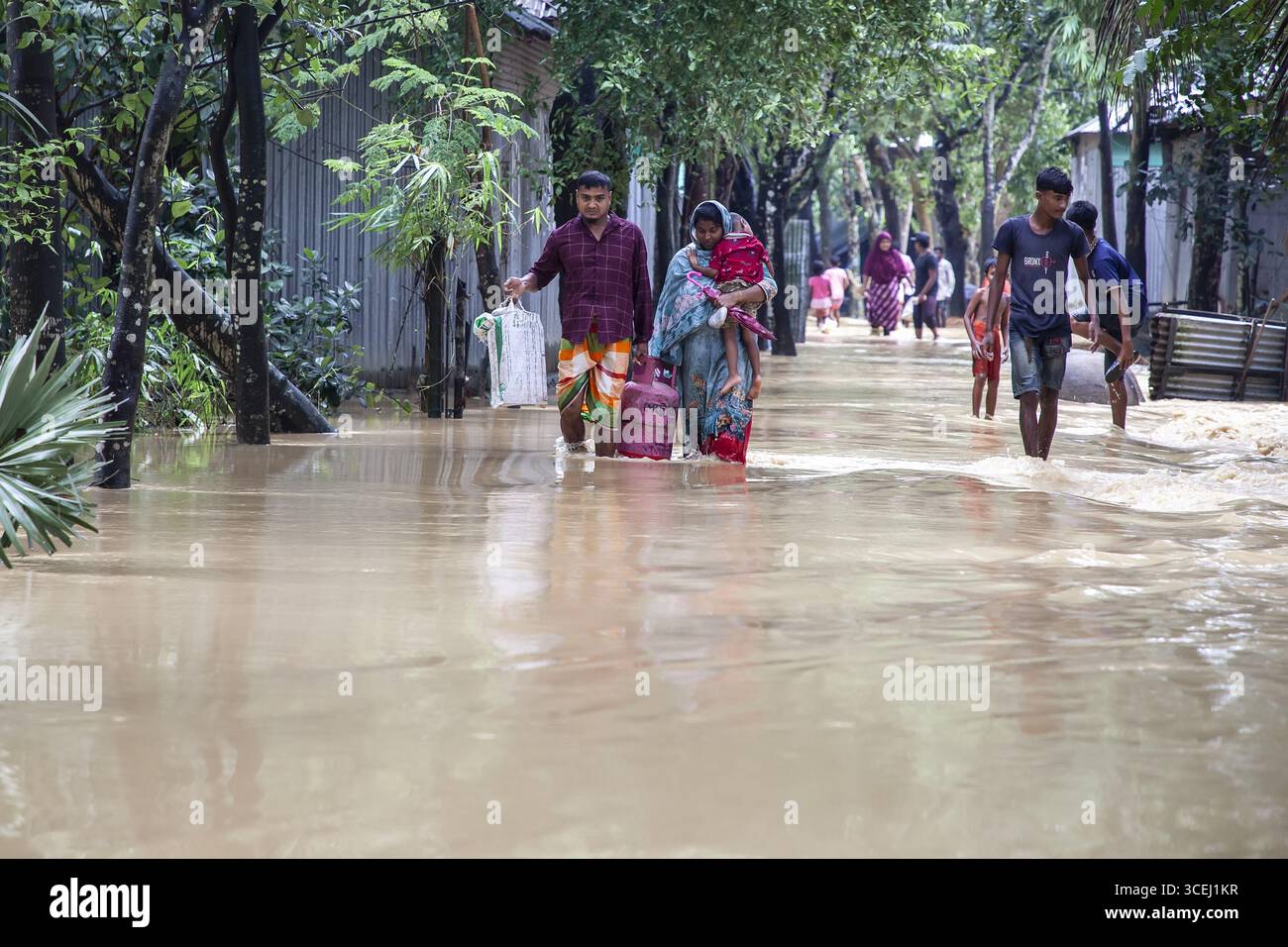 Sherpur, Bangladesh - 06 ottobre 2024: Vista delle famiglie che attraversano le acque alluvionali, case che si riflettono nelle profondità torbide, una scena cupa sotto il cielo coperto. Foto Stock