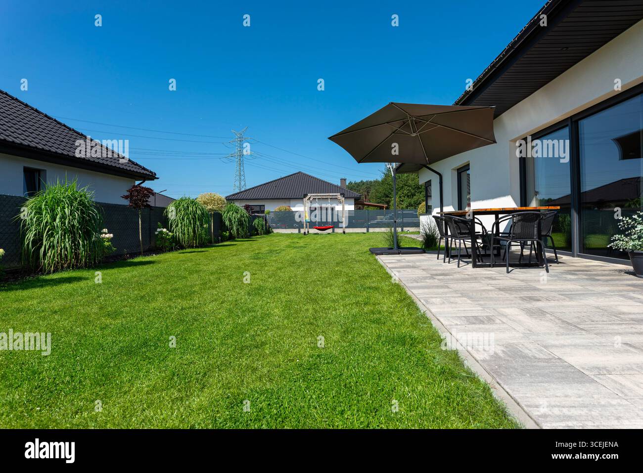 Un bellissimo giardino con erba verde, un tavolo da patio e ombrello visibili, una casa con un bel tempo estivo, un colpo molto ampio. Foto Stock