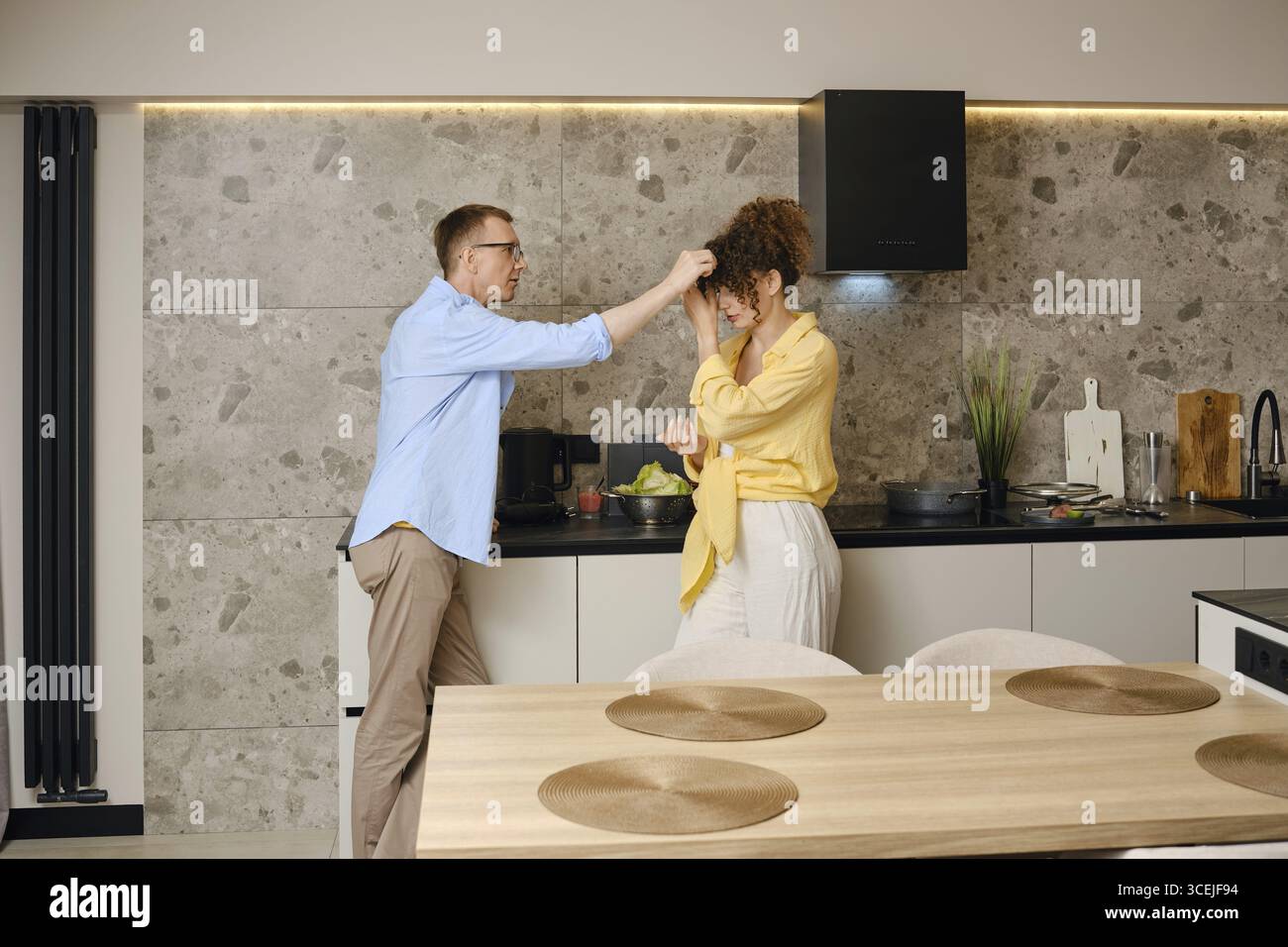 Coppia che si diverte a divertirsi in una cucina moderna mentre preparano un pasto insieme Foto Stock