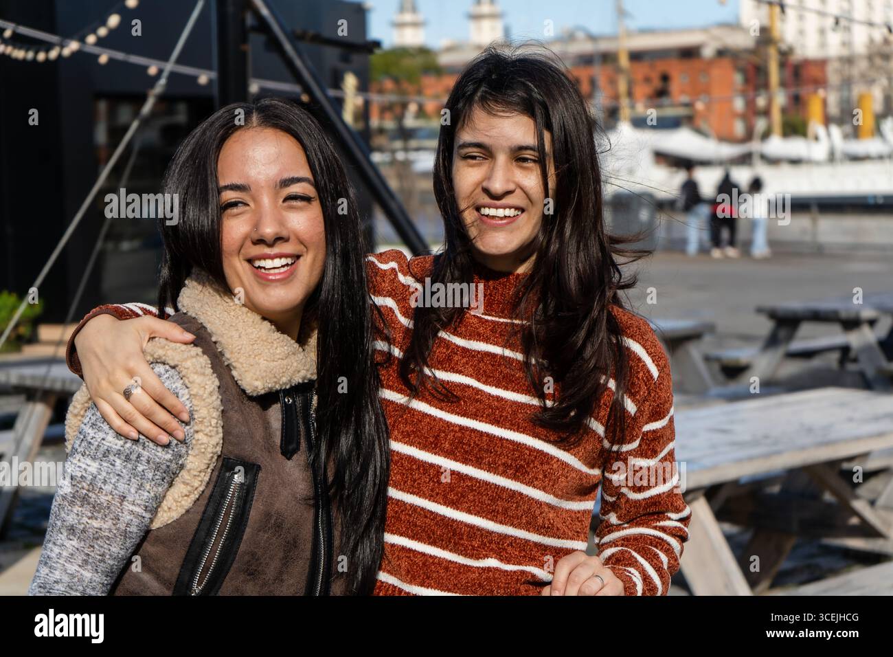 Due amiche felici si stanno abbracciando e sorridendo all'aperto, godendosi una giornata di sole insieme Foto Stock