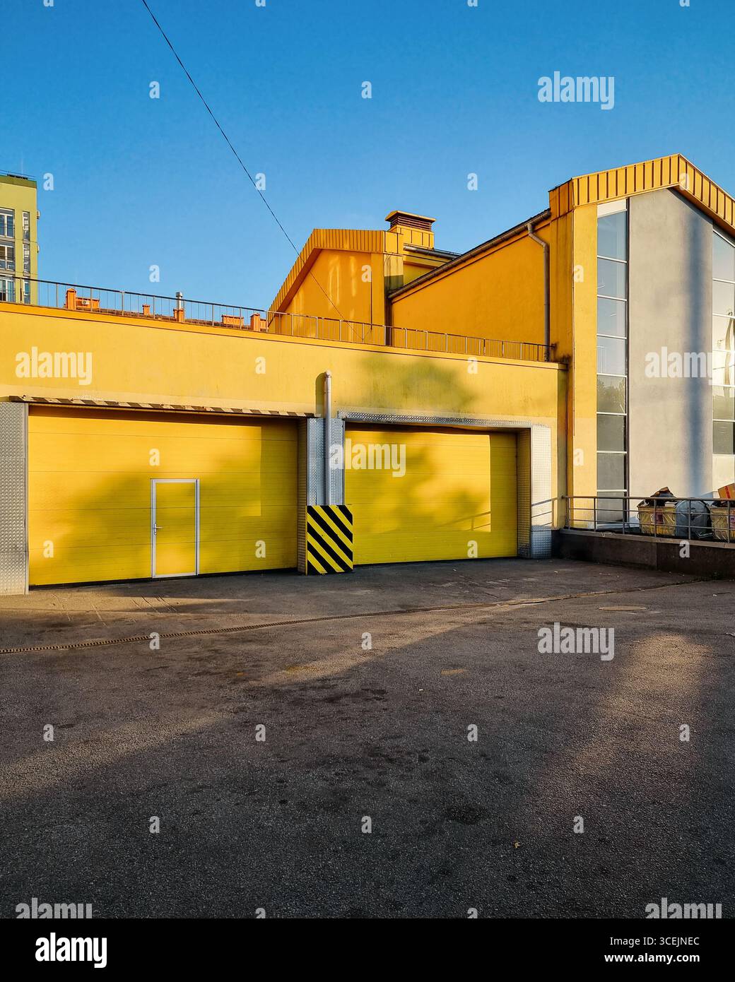 Isolato cittadino con edifici gialli. Strada cittadina con un edificio moderno e luminoso con due cancelli del garage al tramonto. Foto Stock