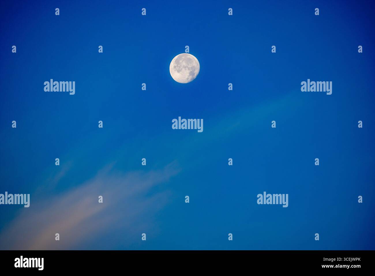 Luna piena che si innalza sopra le nuvole di neve in un cielo notturno blu profondo Foto Stock