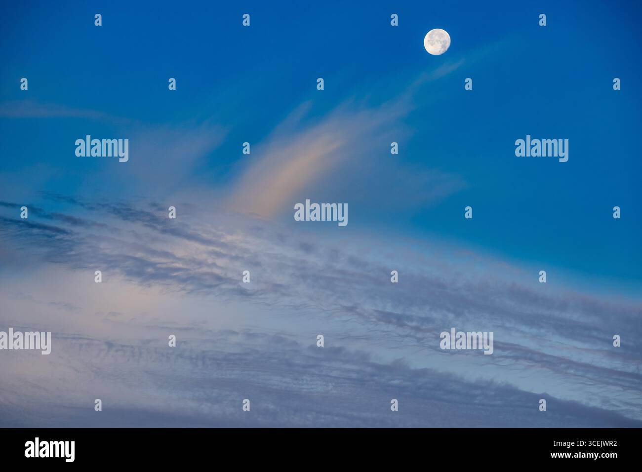 Luna piena che si innalza sopra le nuvole di neve in un cielo notturno blu profondo Foto Stock