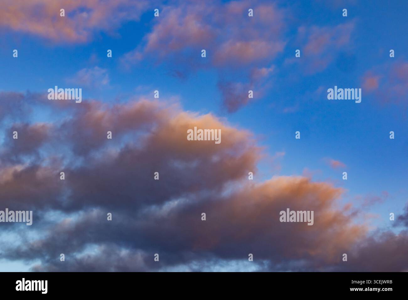 Nuvole spettacolari al tramonto con una luce arancione soffusa contro un cielo blu vivace Foto Stock