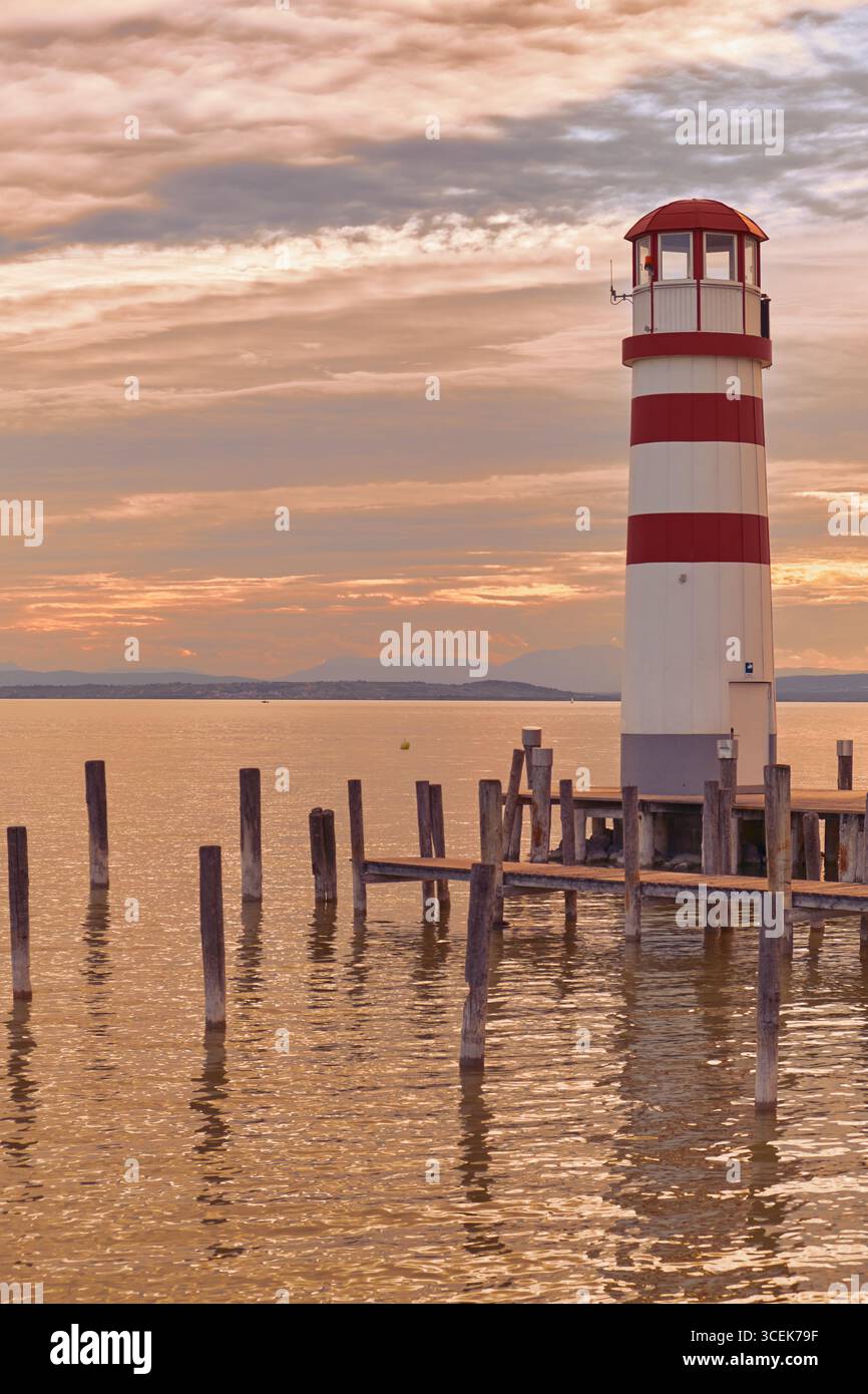 Moli e paletti in legno che si innalzano da Neusiedler SEE con il faro di Podersdorf in lontananza, sotto un caldo cielo color pesca. Foto Stock