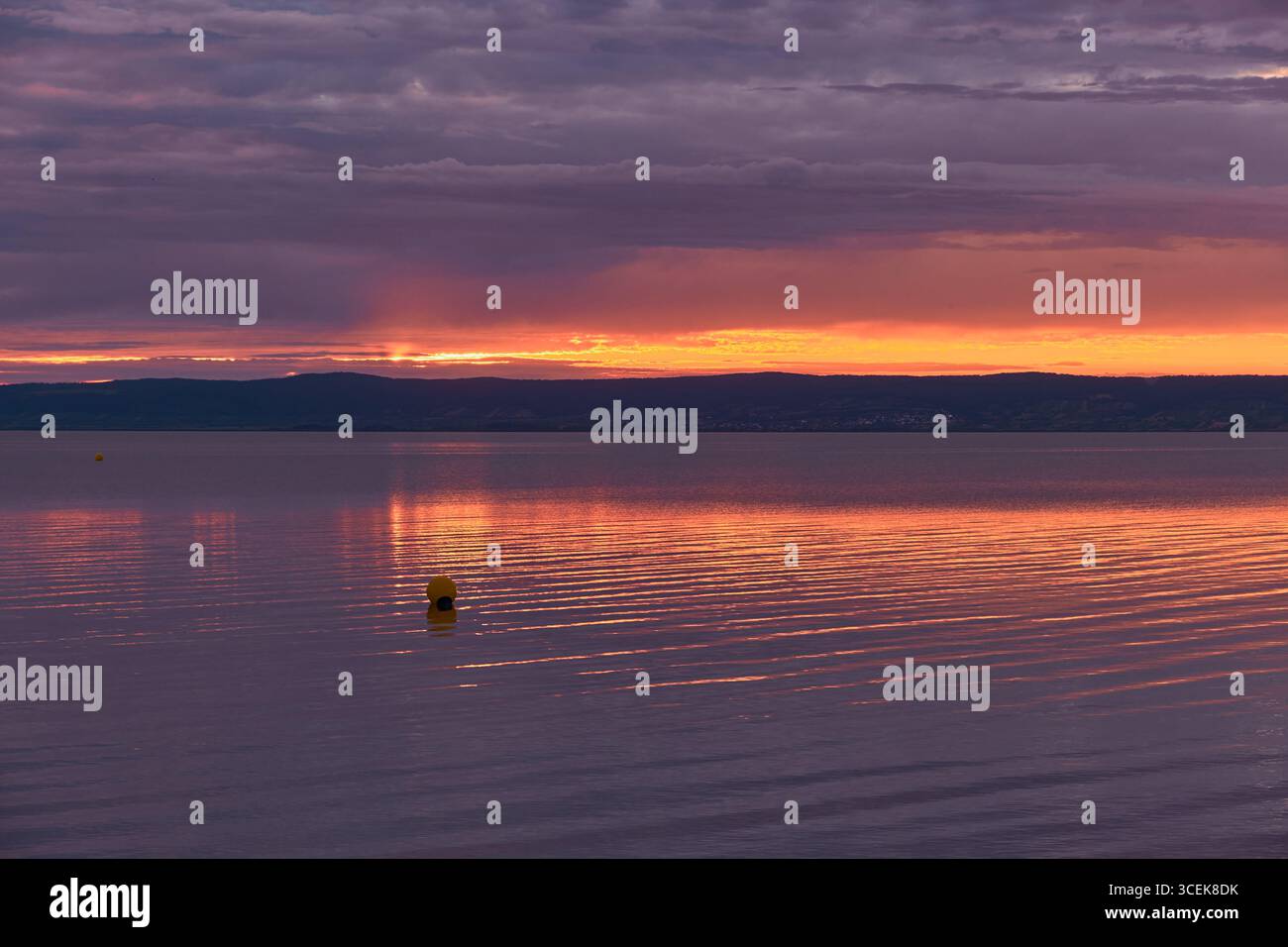 Suggestivo lago di montagna al tramonto con nuvole viola, riflessi arancioni luminosi sull'acqua, calmo galleggiante sulla superficie calma. Foto Stock