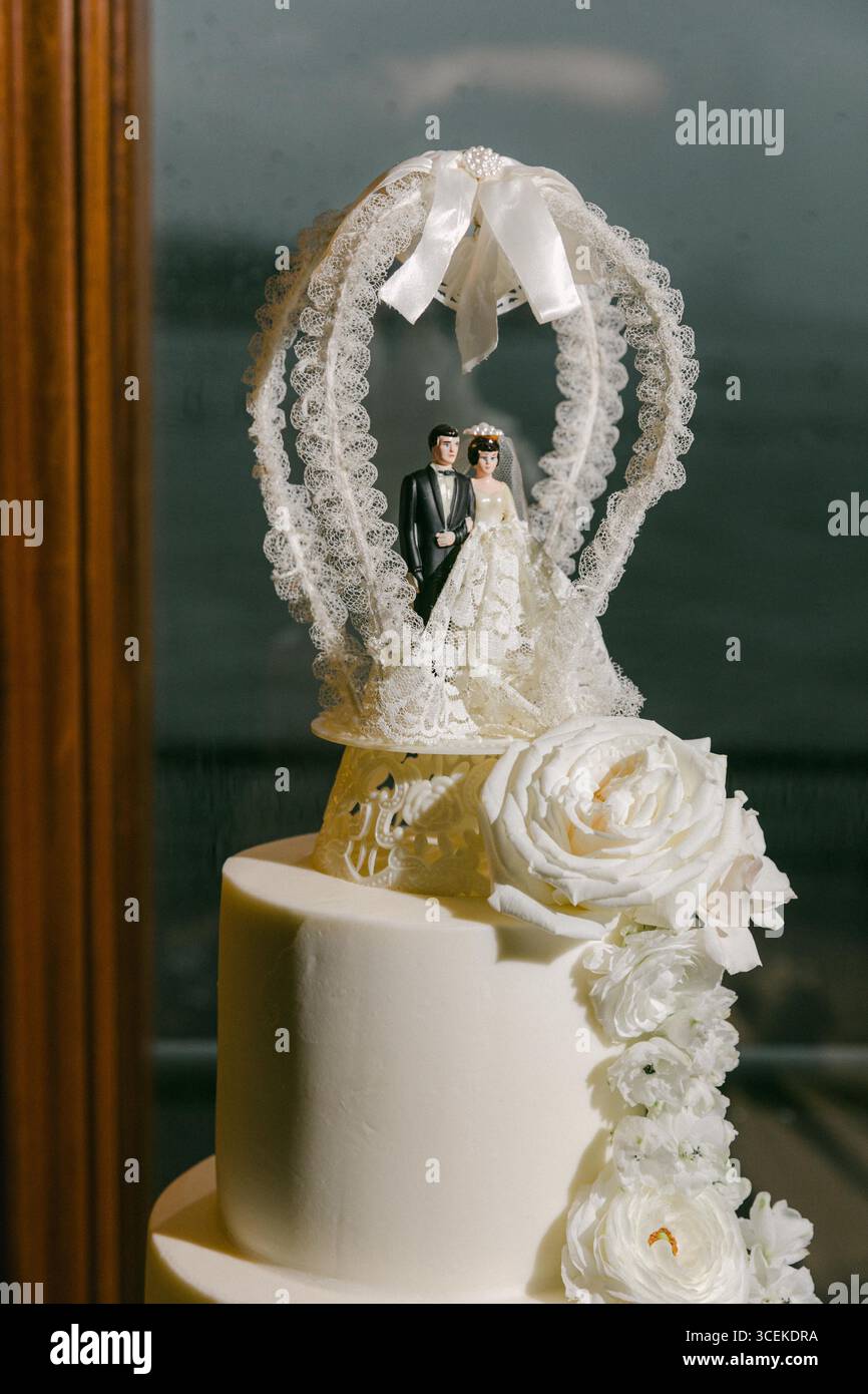 Una splendida torta nuziale con pizzo e dettagli floreali aggiunge romanticismo a un ambiente costiero. Foto Stock