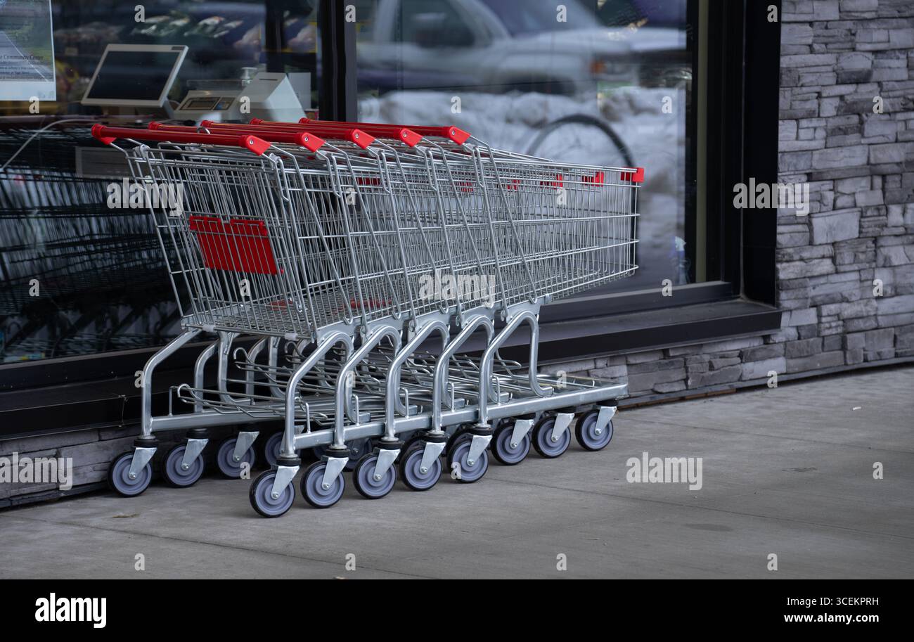 cinque carrelli vuoti insieme all'esterno del negozio di alimentari in acciaio inossidabile con ruote e maniglie rosse impilate insieme all'esterno del negozio di alimentari Foto Stock