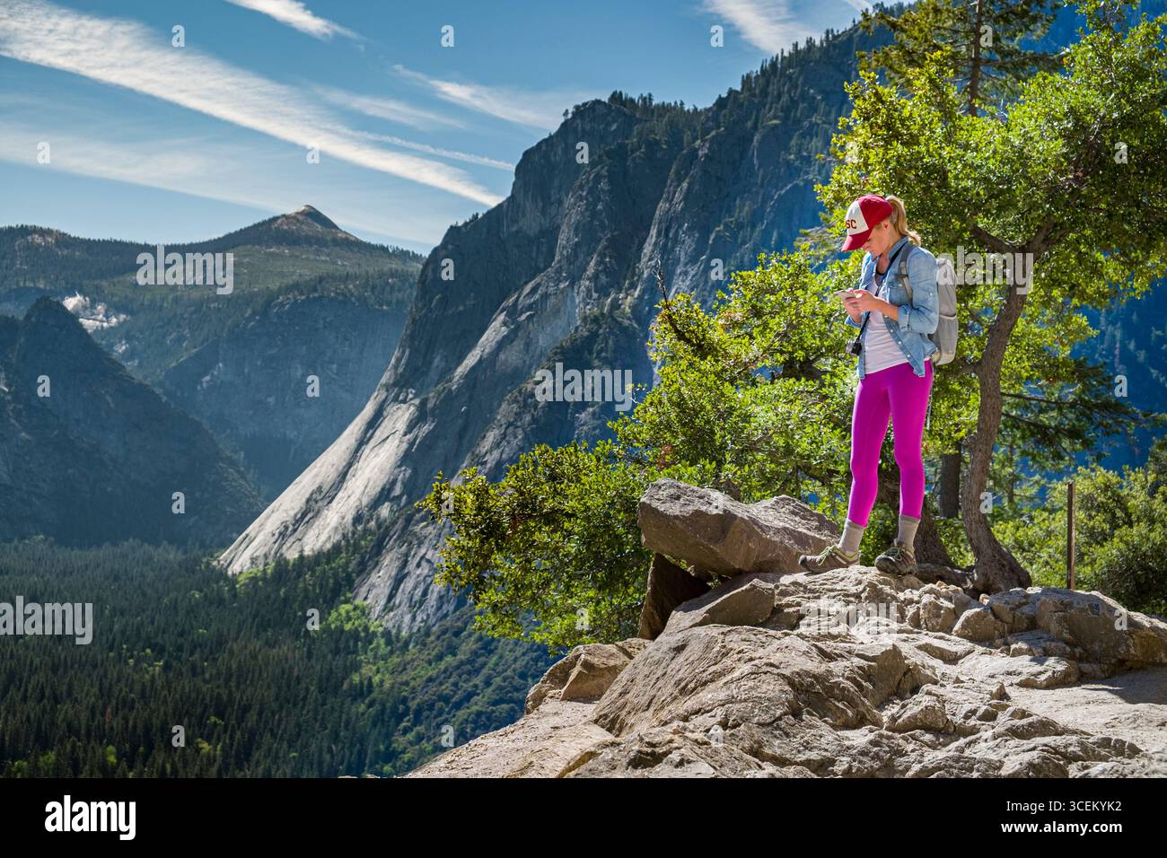 Giovane donna caucasica invio di testo dal suo IPhone telefono cellulare con Yosemite Valley in background, del Parco Nazionale Yosemite, di Mariposa County, Foto Stock