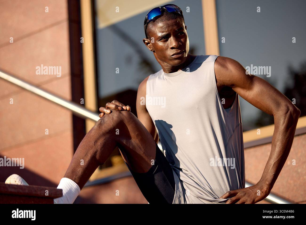 Un uomo in forma e muscoloso si prende una pausa dopo la sua routine di allenamento. Posato su una scala esterna, indossa un abbigliamento da allenamento, tra cui una camicia senza maniche A. Foto Stock
