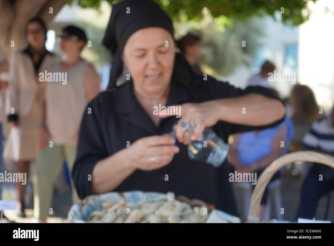Creta, Grecia, 3 agosto 2025. Uno sfondo sfocato di una donna che versa raki, ideale per argomenti sull'ospitalità e la tradizione cretese. Foto Stock