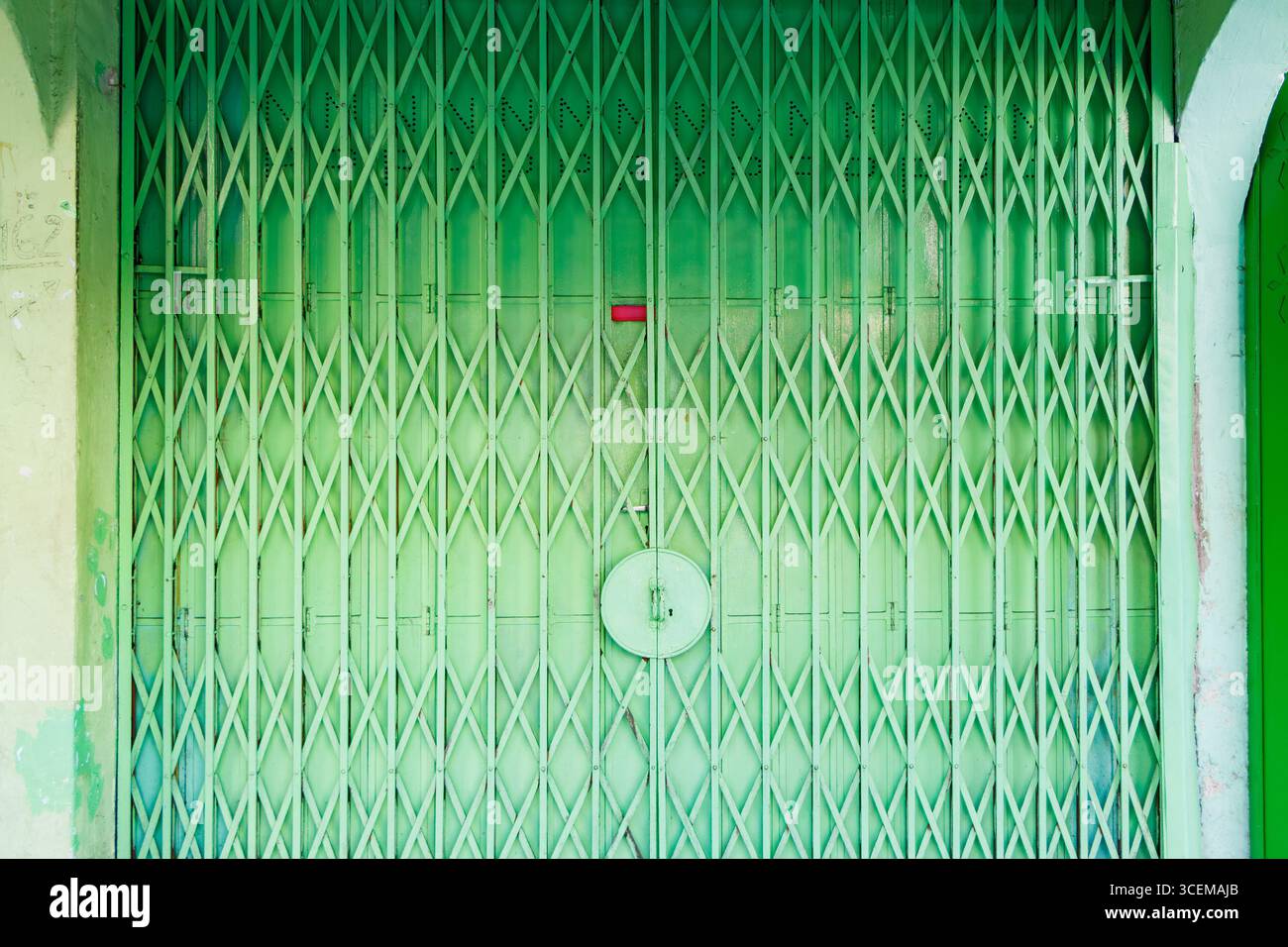 Cancello di sicurezza in stile fisarmonica in metallo verde rustico con lucchetto circolare e negozio di etichette rosse George Town Penang Malesia Foto Stock
