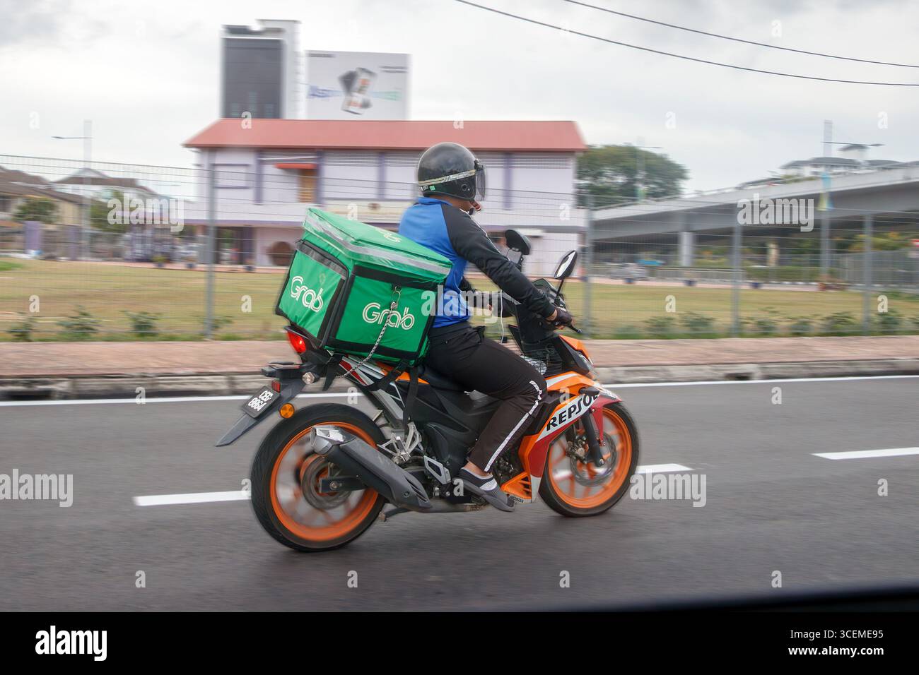 Corriere motociclistico che consegna il cibo in bicicletta lungo una strada urbana con edifici e vegetazione sullo sfondo George Town Penang Island malesia Foto Stock